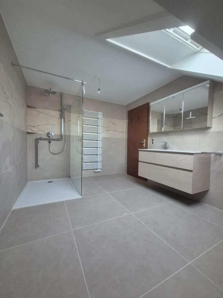 Modernisierte Badrenovierung nach Rohrbruch mit großformatigen beigefarbenen Fliesen und neuer Dusche als Versicherungsfall